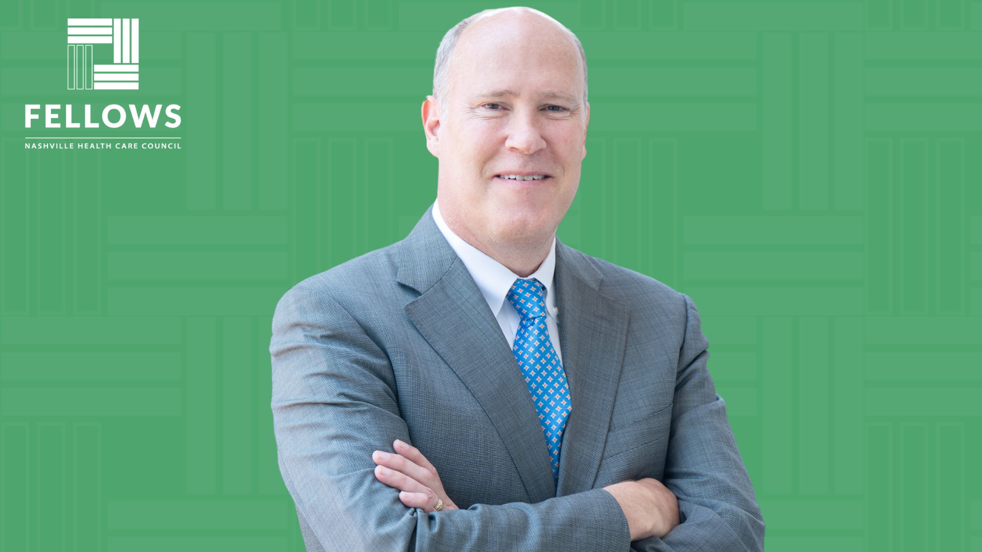 Morgan Wills, a man in a business suit with a blue tie stands with arms crossed in front of a green background, featuring the "Nashville Health Care Council Fellows" logo 
